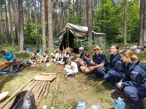policjanci rozmawiają z harcerzami w tle las i namioty