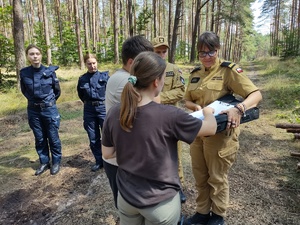 policjanci rozmawiają z harcerzami w tle las i namioty