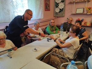 policjanci rozmawiają z seniorami w tle pomieszczenie PZN