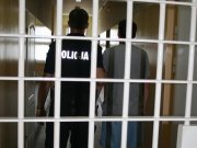 kraty więzienne za nim policjant i osoba zatrzymana