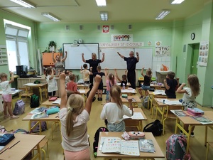 policjanci rozmawiają z dziećmi w tle sala lekcyjna i uczniowie