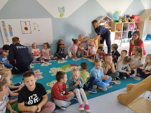 policjant i miś uczą dzieci pierwszej pomocy w tle sala