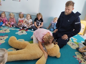 policjant i miś uczą dzieci pierwszej pomocy w tle sala