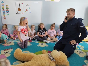 policjant i miś uczą dzieci pierwszej pomocy w tle sala
