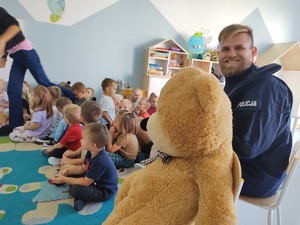 policjant i miś uczą dzieci pierwszej pomocy w tle sala