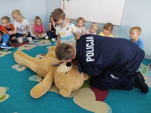 policjant i miś uczą dzieci pierwszej pomocy w tle sala