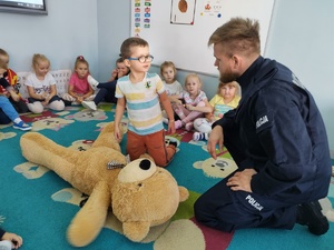 policjant i miś uczą dzieci pierwszej pomocy w tle sala