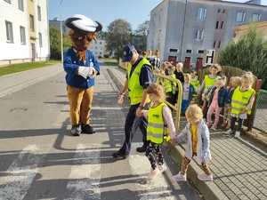 policjanci uczą dzieci chodzić po ulicy w tle ulica i maskotka policyjna