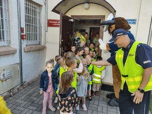 policjanci uczą dzieci chodzić po ulicy w tle ulica i maskotka policyjna
