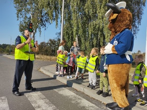 policjanci uczą dzieci chodzić po ulicy w tle ulica i maskotka policyjna