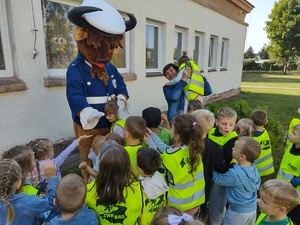 policjanci uczą dzieci chodzić po ulicy w tle ulica i maskotka policyjna