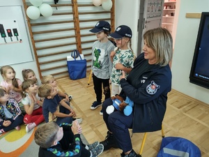 policjanci rozmawiają z przedszkolakami w tle sala i dzieci