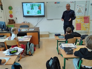 policjant rozmawia z uczniami w tle tablica