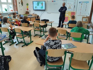 policjant rozmawia z uczniami w tle tablica
