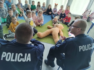 policjanci uczą dzieci pierwszej pomocy w tle sala