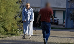 kobieta idzie w szlafroku przed nią mężczyzna w tle zabudowania