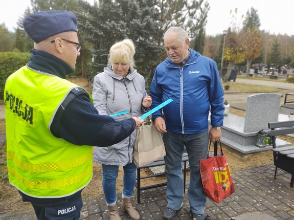 policjanci wręczają odblaski w tle cmentarz