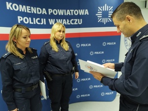 Komendant wręcza awanse w tle ścianka z logo policji
