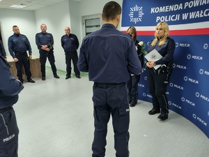 Komendant wręcza awanse w tle ścianka z logo policji