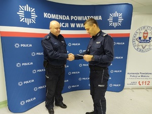 komendant wręcza wyróżnienie w tle ścianka z logo policji