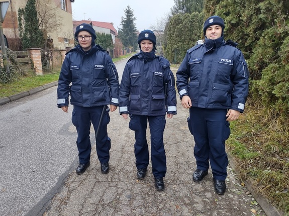 policjanci idą drogą w tle zabudowania