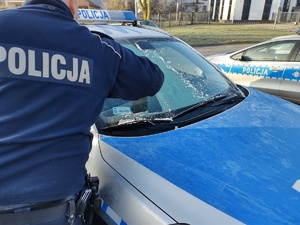 policjant oczyszcza auto z lodu w tle inny radiowóz