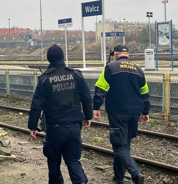 policjant i strażnik miejski kontrolują dworzec, w tle tory