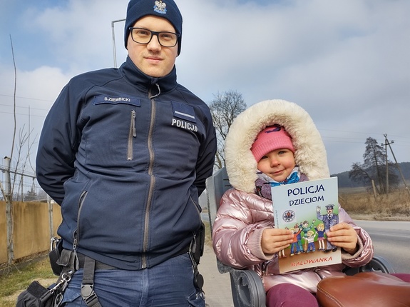 policjant wręcza dziecku kolorowankę w tle ulica