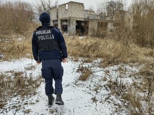 policjant kontroluje pustostan w tle zarośla i opuszczony budynek