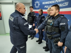 komendant wręcza nagrody policjantom w tle baner i ściany w pomieszczeniu