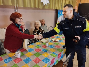 policjant wręcza seniorce torbę w tle inni seniorzy