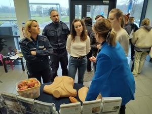 przedstawiciel NFZ rozmawia z policjantami i innymi osobami, w tle hol komendy