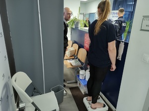 przedstawiciel NFZ rozmawia z policjantami i innymi osobami, w tle hol komendy