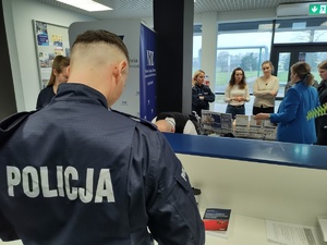 przedstawiciel NFZ rozmawia z policjantami i innymi osobami, w tle hol komendy