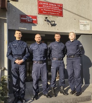 policjanci przed wejściem do budynku internatu w tle wejście i tablica informacyjna