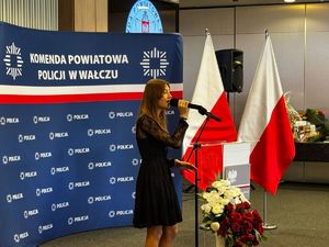 kobieta trzyma w ręce mikrofon i śpiewa w tle ścianka z napisem policja