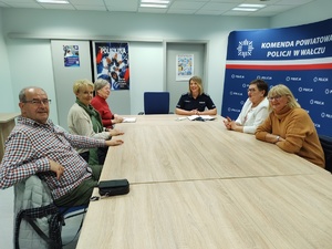 policjantka rozmawia z seniorami, wszyscy siedzą przy stole w tle wyposażenie sali