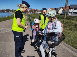 policjanci wręczają odblaski rowerzystom w tle promenada jeziora