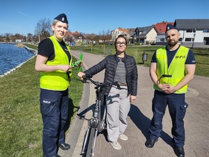 policjanci wręczają odblaski rowerzystom w tle promenada jeziora