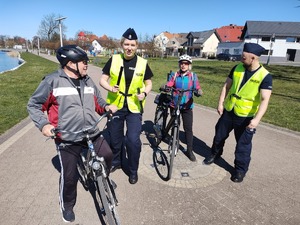 policjanci wręczają odblaski rowerzystom w tle promenada jeziora