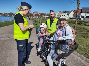 policjanci wręczają odblaski rowerzystom w tle promenada jeziora