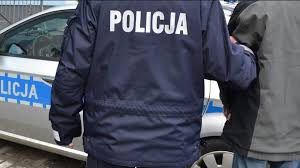 policjant prowadzi zatrzymanego w tle radiowóz