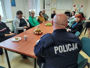 policjant rozmawia z seniorami w tle sala