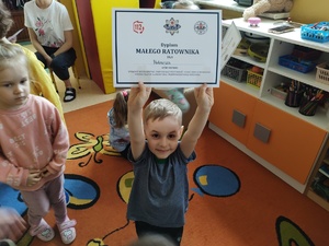chłopiec chwali się otrzymanym dyplomem w tle dzieci