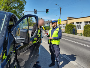 policjant sprawdza stan trzeźwości u kierowcy w tle ulica z sygnalizacją świetlną  i pojazdy