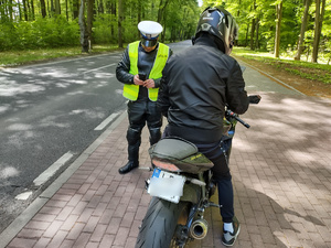 policjant kontroluje motocyklistę w tle las i droga