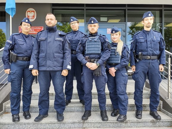 policjanci stoją na schodach przed wejściem do budynku komendy w tle wejście i tablica informacyjna