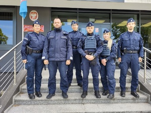 policjanci stoją na schodach przed wejściem do budynku komendy w tle wejście i tablica informacyjna
