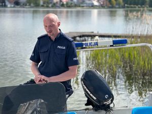 policjant stoi na łodzi w tle jezioro