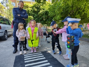 policjant uczy dzieci prawidłowych zachowań na drodze w tle teren przedszkola